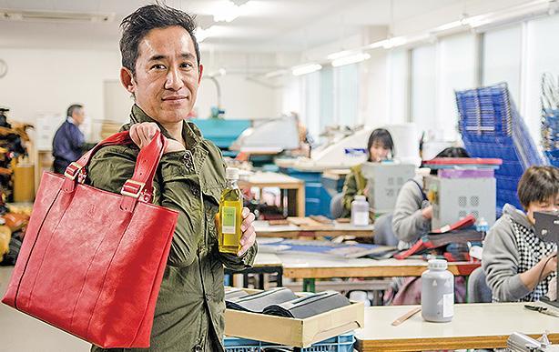 オリーブオイルで仕上げたWOGNAブランドのバッグを持つ長田さん＝東かがわ市川東のエールック縫製工場