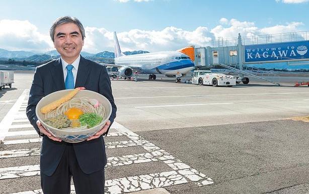 高松空港名物「特大讃岐うどん」（模型）を手にする渡部社長＝高松市香南町の高松空港