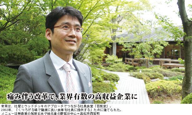 背景は、社屋とウッドデッキのアプローチでつながる社員食堂「百菜家」。2002年、「くつろげる場で健康に良い食事を社員に提供する」ために建てられた。メニューは無農薬の発芽玄米や地元産の野菜が中心＝高松市西宝町